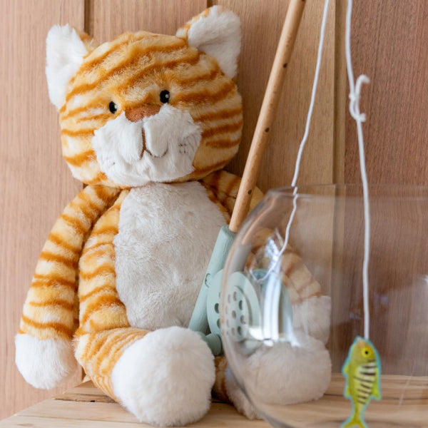 Plush tiger toy with fishing rod and glass jar on wooden surface
